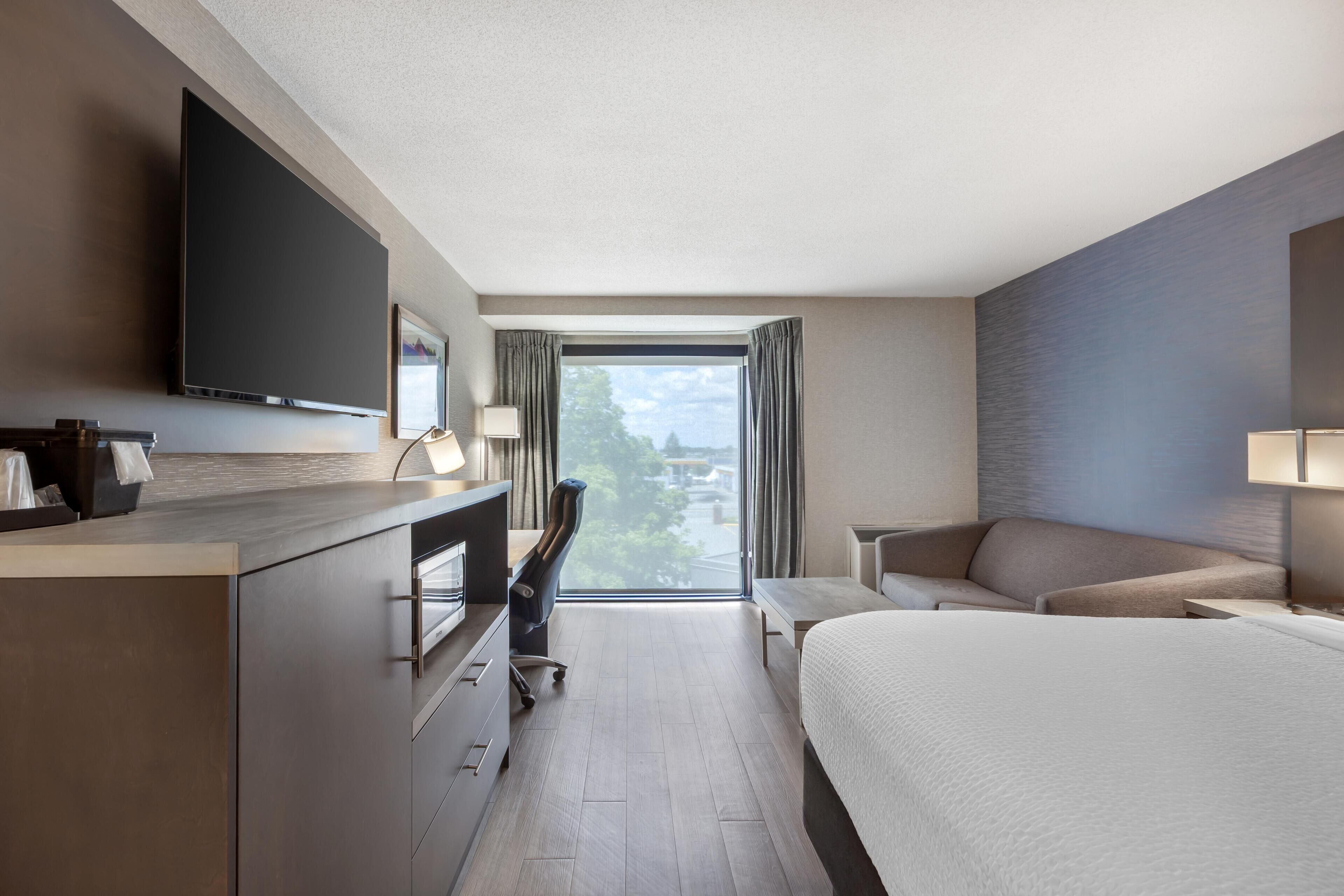 Een hotelkamer met een bed, bureau, stoel, televisie en uitzicht op het groen.