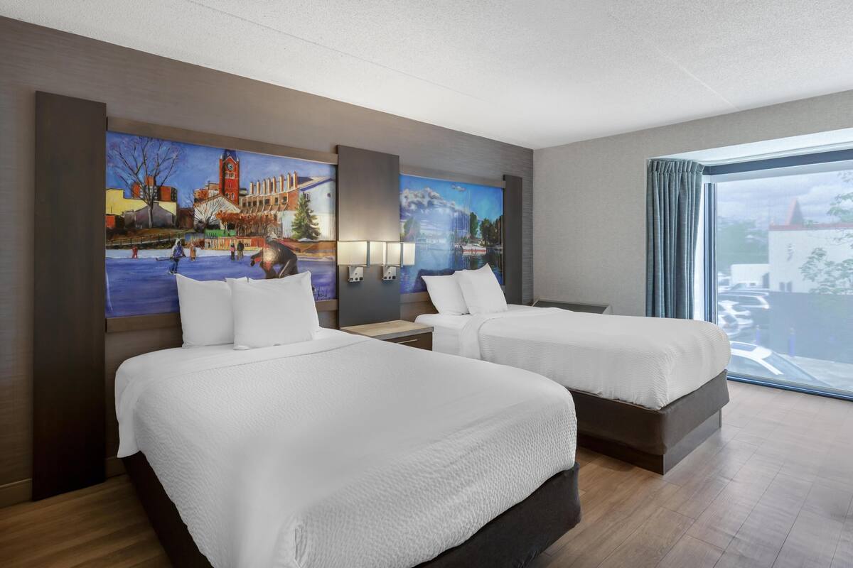 A hotel room with two beds, a large window, and a mural on the wall.
