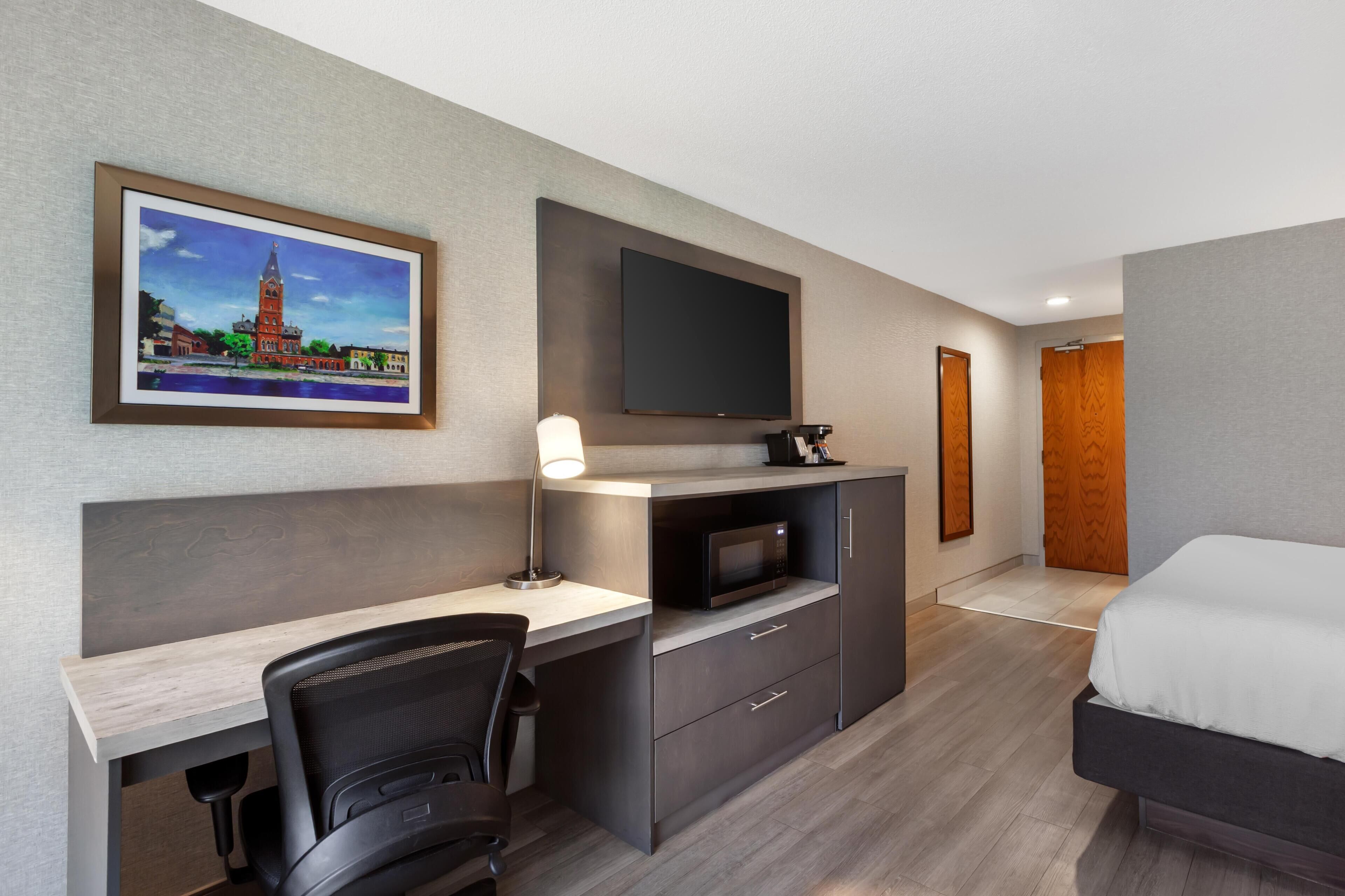 Habitación de hotel con cama, escritorio, silla, televisión y un cuadro en la pared.