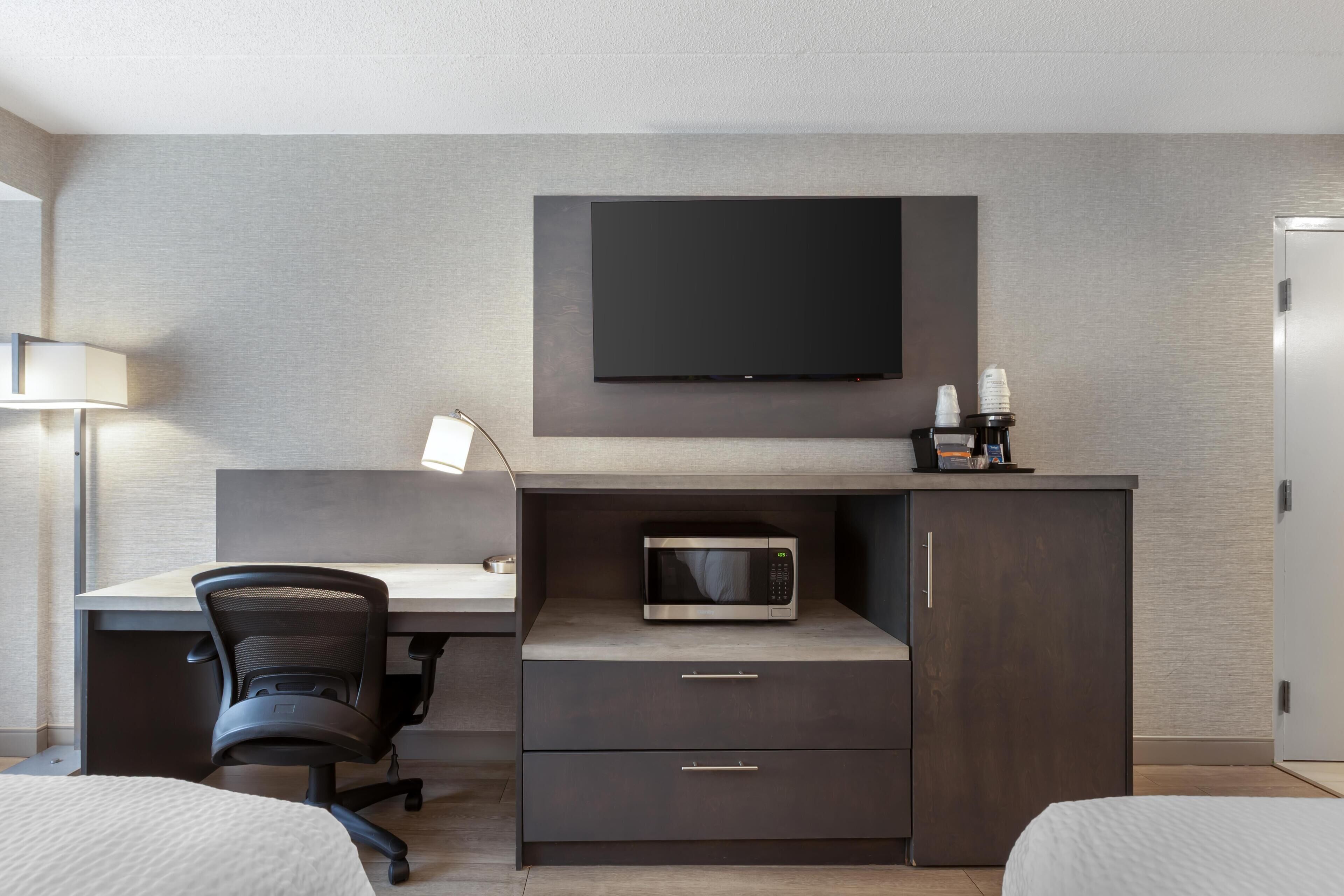 Una habitación de hotel moderna con televisión de pantalla plana, microondas, escritorio con silla y cama.