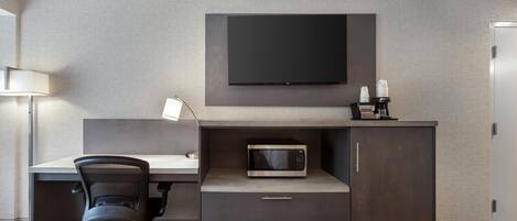 A modern hotel room with a flat-screen TV, a microwave, a desk with a chair, and a bed.