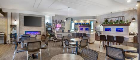 Un hall d’hôtel moderne doté d’un bar, de différents espaces de détente et d’un grand écran de télévision.