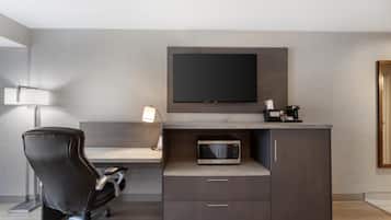 Een moderne hotelkamer met een bureau, een stoel, een wandtelevisie, een magnetron en een klein kastje.
