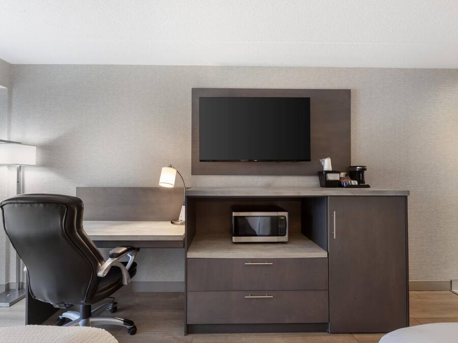 Een moderne hotelkamer met een bureau, een stoel, een wandtelevisie, een magnetron en een klein kastje.