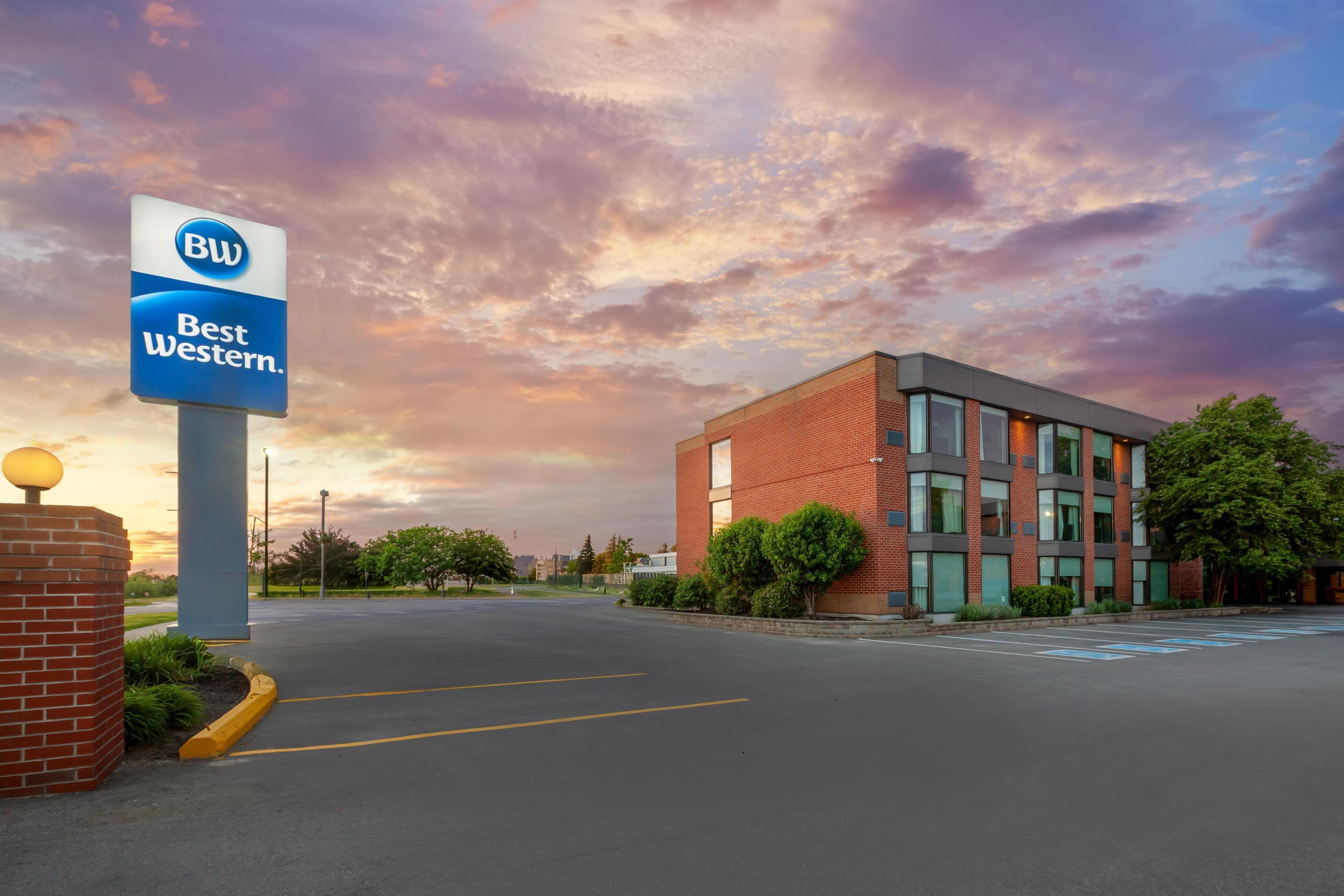 Un hotel Best Western con un edificio moderno de ladrillo, un estacionamiento y un cielo despejado.