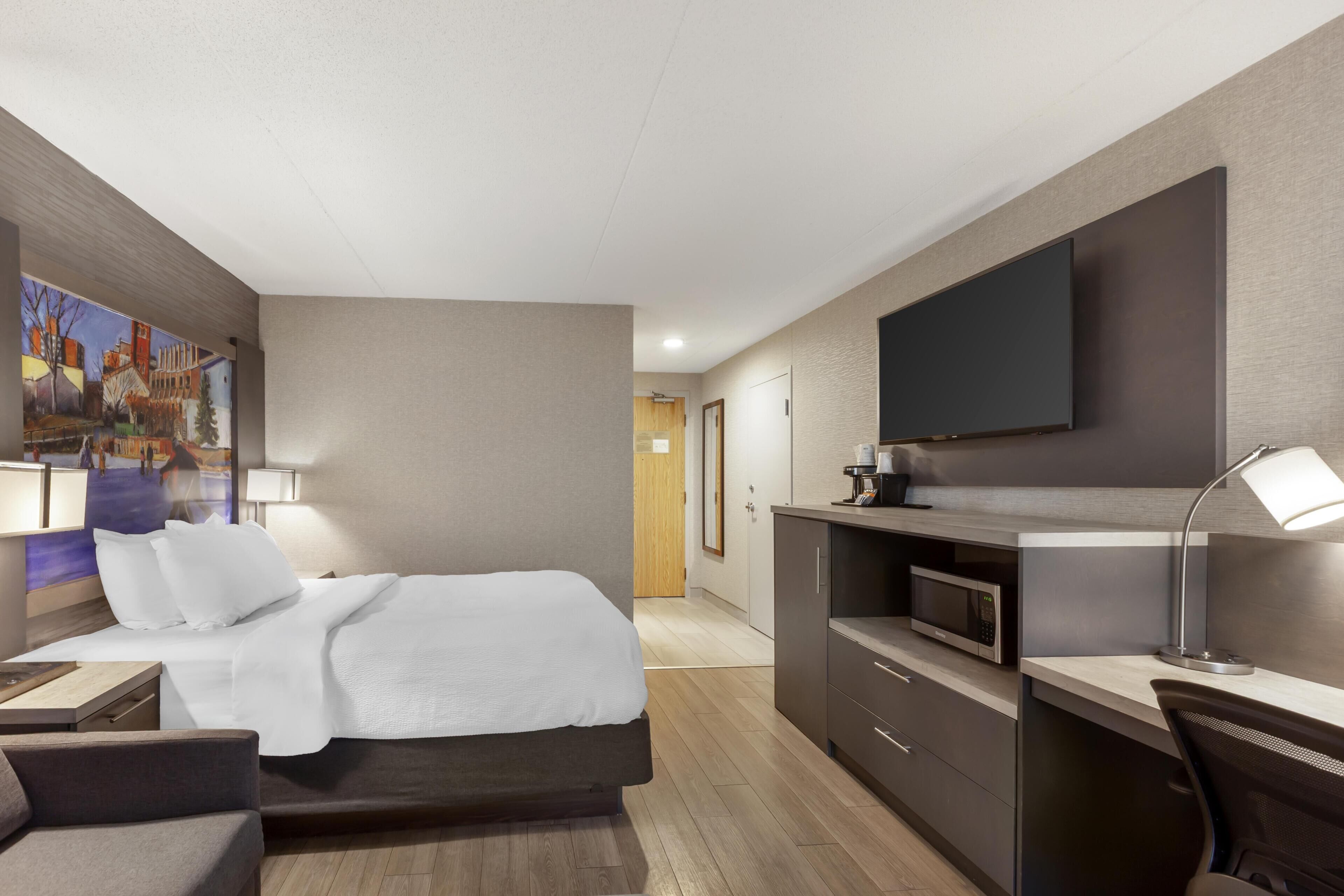A hotel room with a bed, desk, chair, TV, and a painting on the wall.