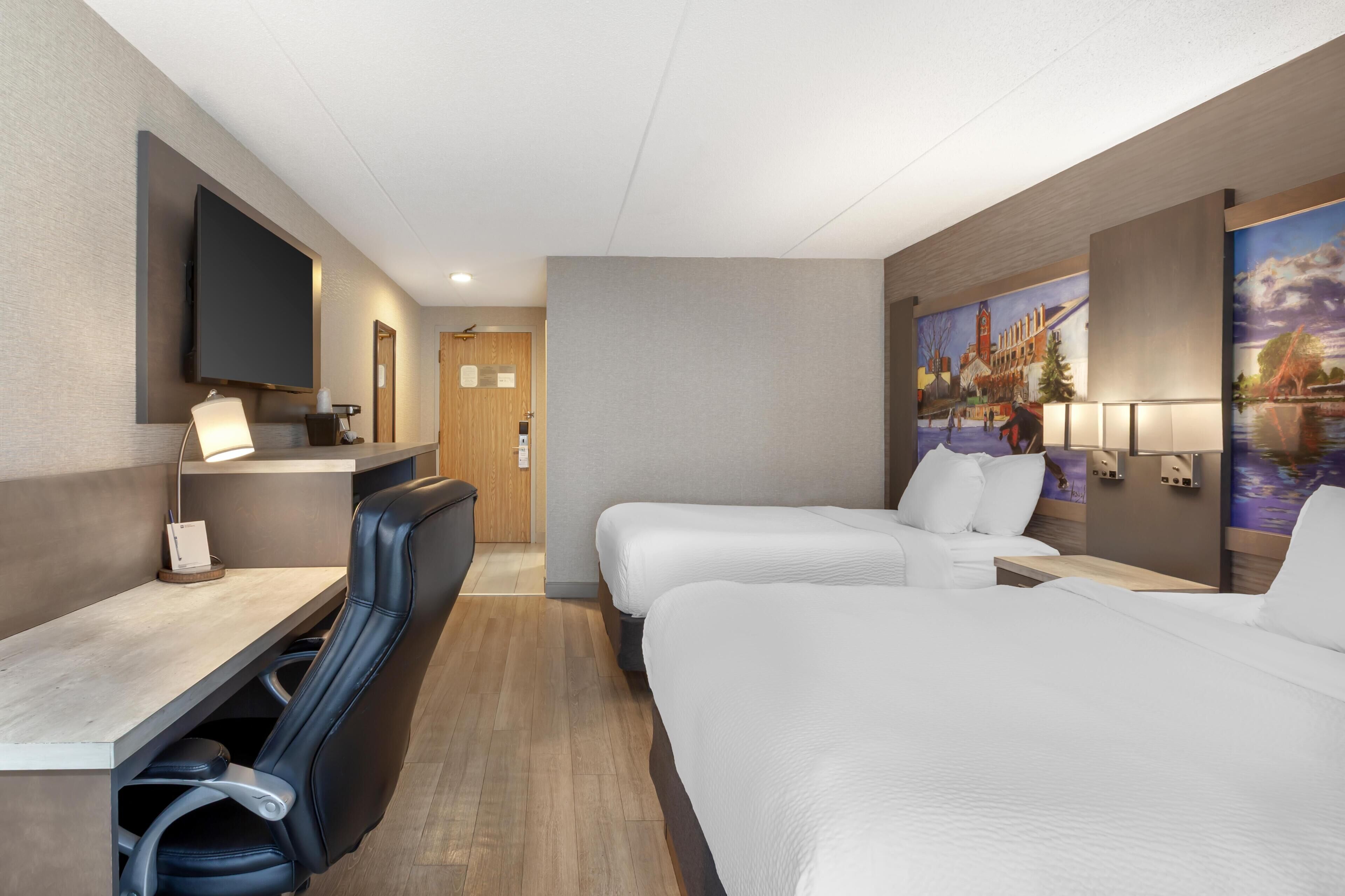 Una habitación de hotel con escritorio, dos camas, televisor y un cuadro en la pared.