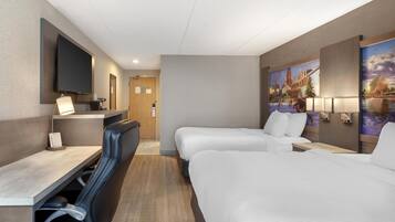 Una habitación de hotel con escritorio, dos camas, televisor y un cuadro en la pared.