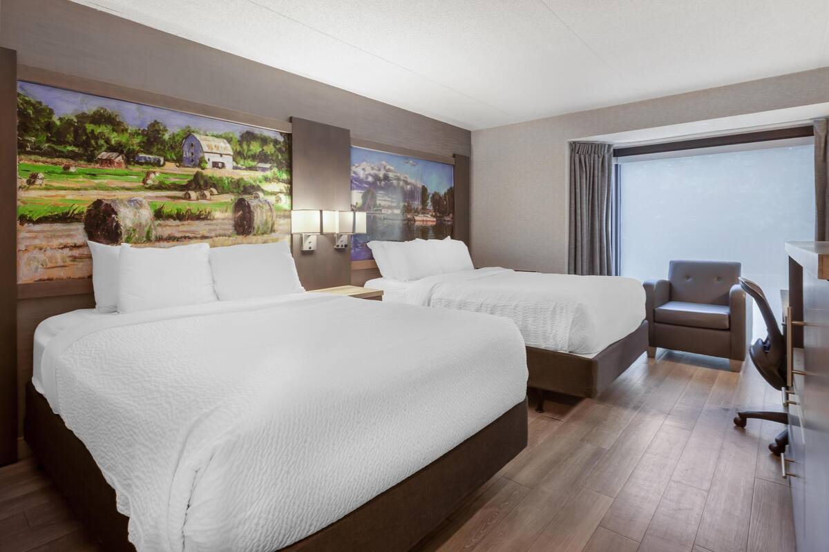 A hotel room with two beds, a desk, a chair, and a large window.