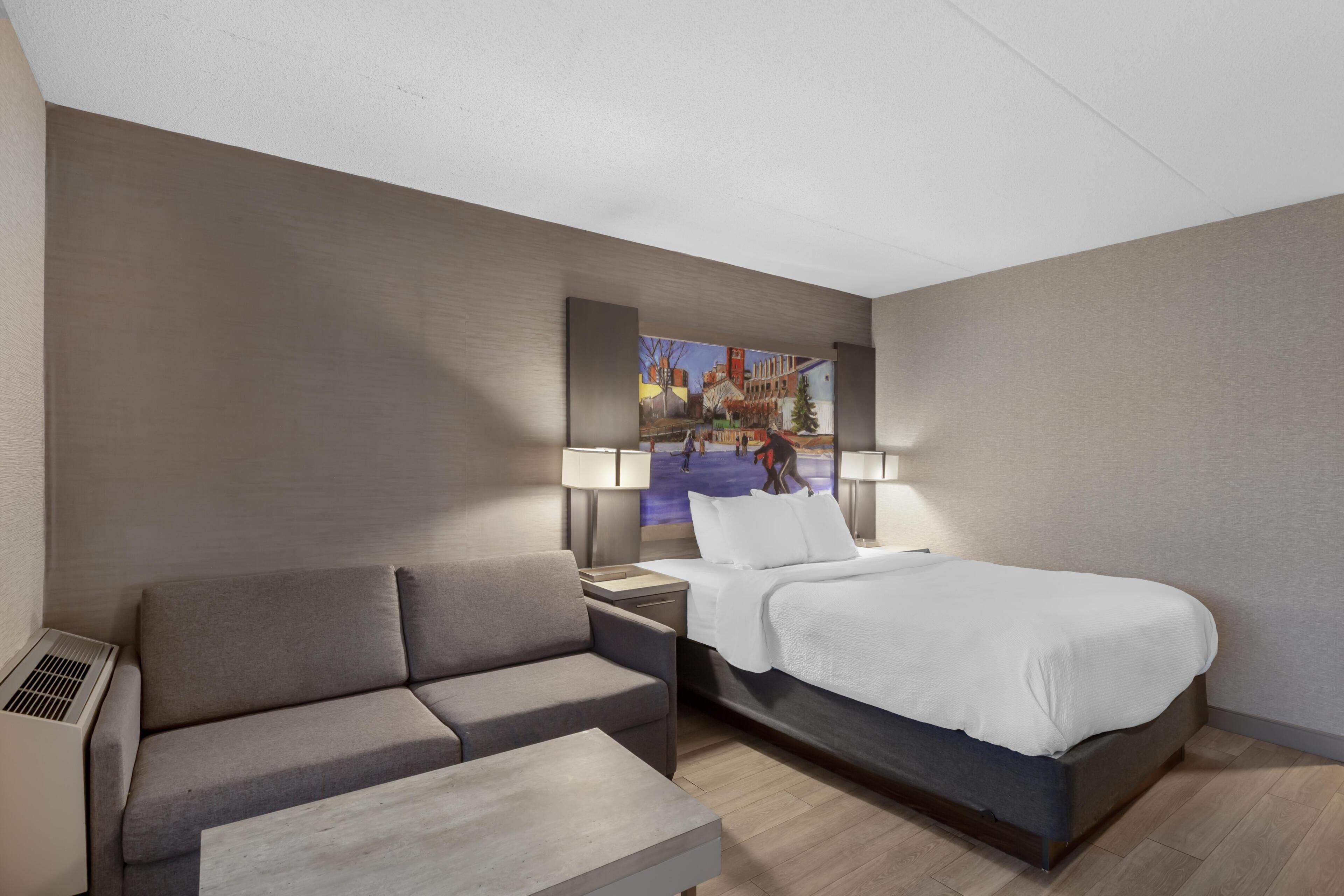 A hotel room with a bed, a sofa, a small table, and a wall-mounted TV.