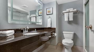A modern bathroom with a dark marble countertop, a large mirror, a white toilet, and a towel rack.