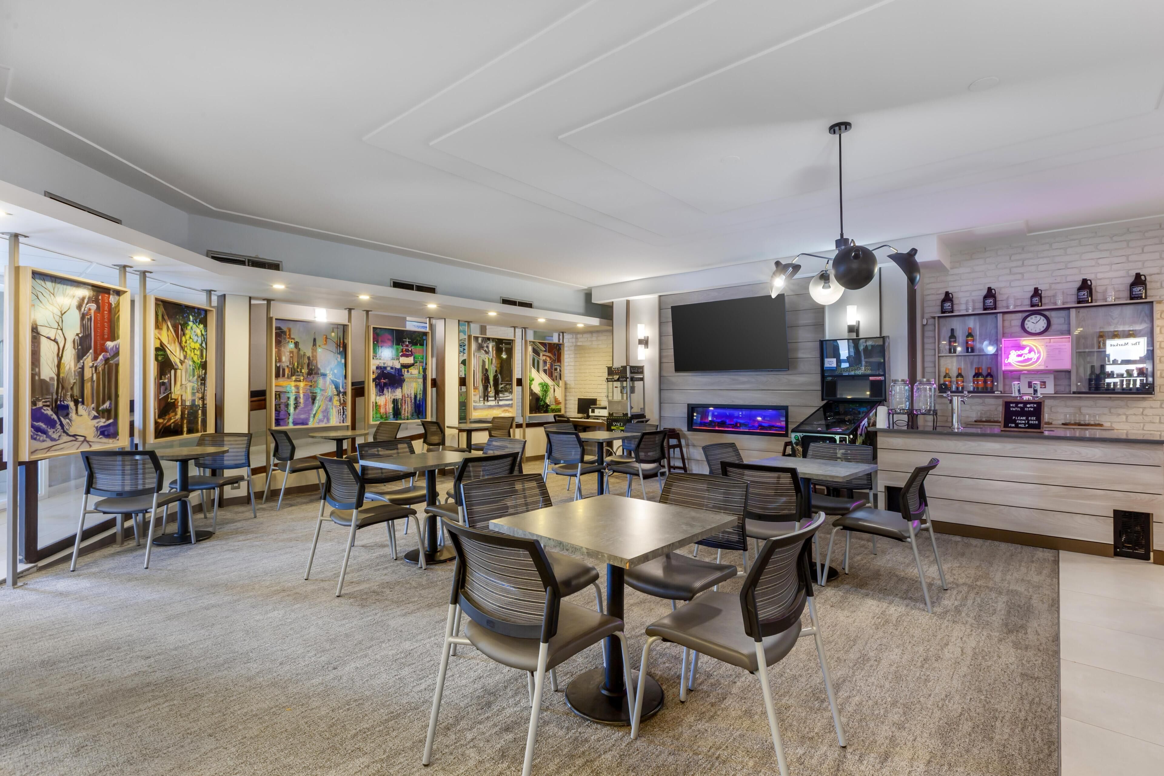 A modern restaurant with multiple tables and chairs, a bar area, and artwork on the walls.