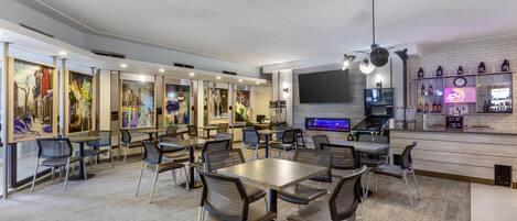 Un restaurante moderno con varias mesas y sillas, una zona de bar y obras de arte en las paredes.
