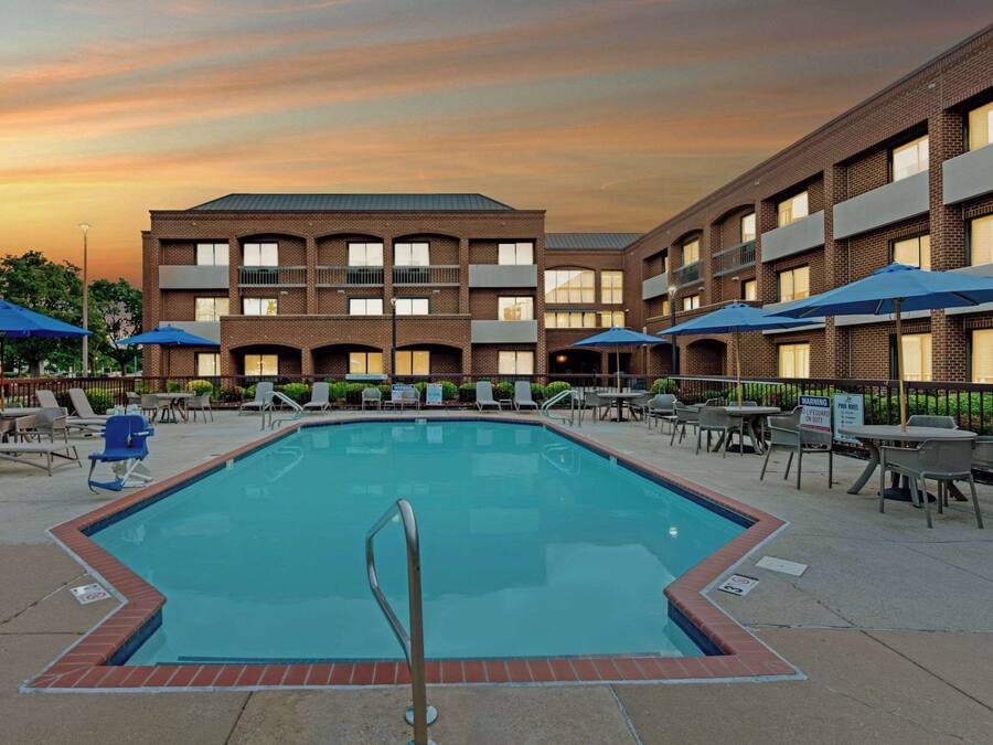 A swimming pool with lounge chairs and umbrellas, surrounded by a building with multiple balconies.