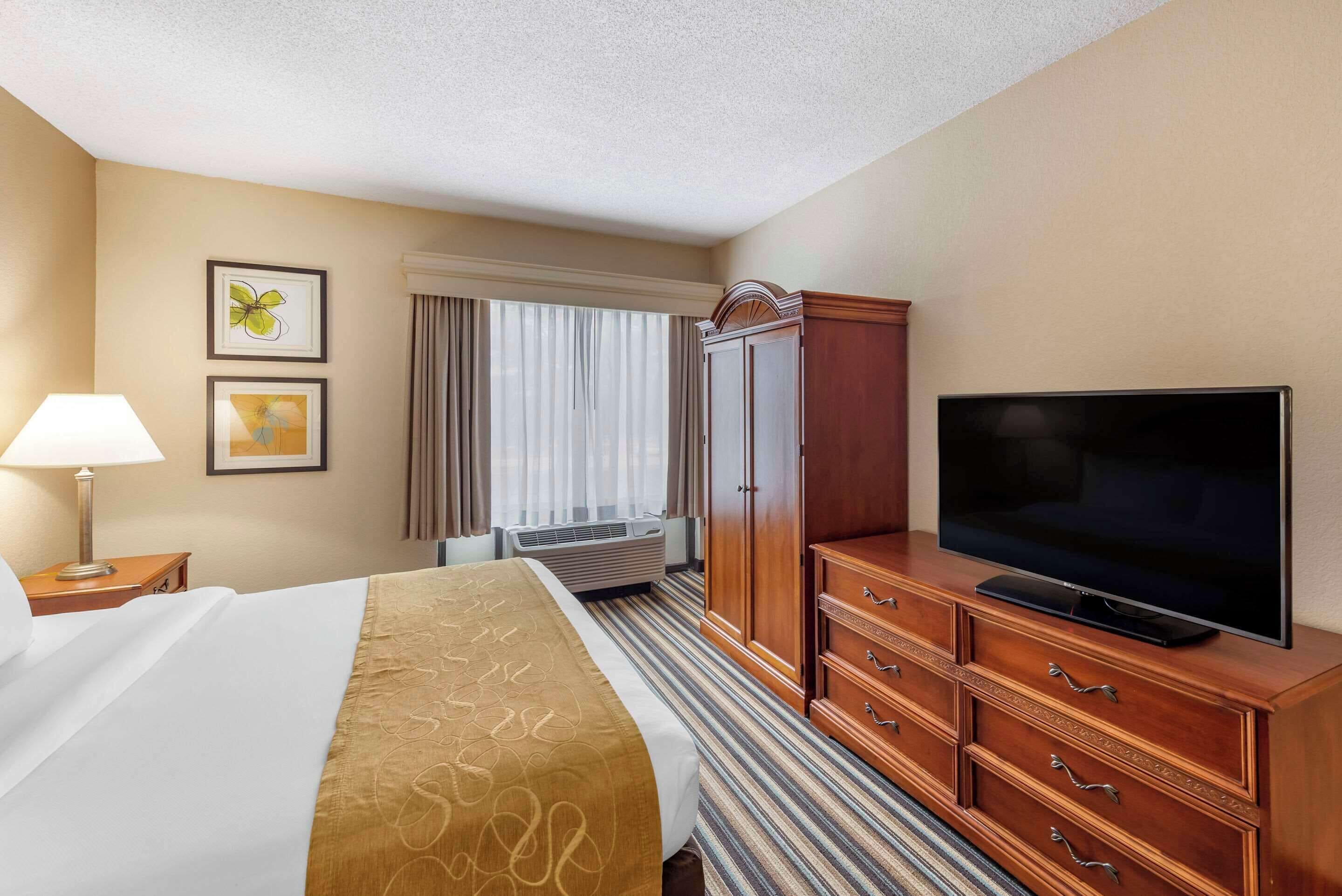 Una habitación de hotel con cama, televisión, armario y ventana con cortinas.