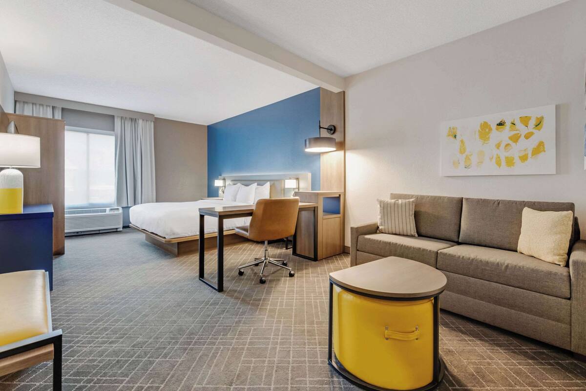 A hotel room with a bed, a desk, a chair, a sofa, and a small table.