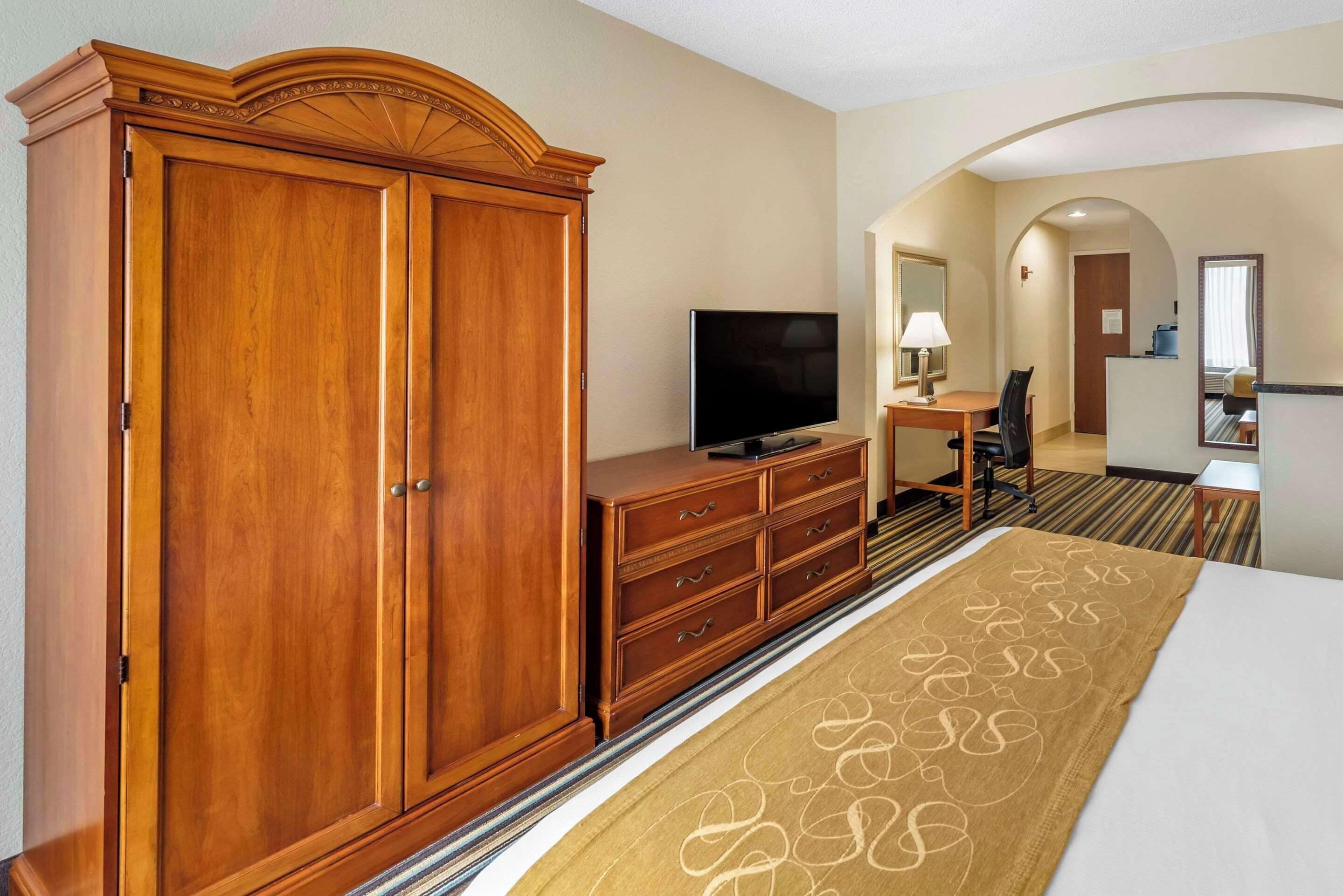 Hotelkamer met een grote houten garderobe, een flatscreen-televisie, een bureau met lamp en een bed met een decoratieve loper.