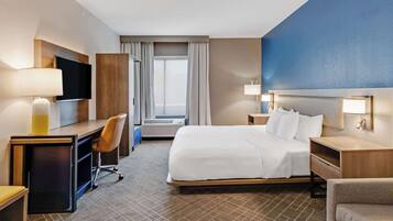 A hotel room with a bed, desk, chair, TV, and a large window.