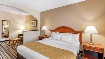 A hotel room with a large bed, two bedside tables with lamps, a wooden headboard, a striped carpet, and a wall-mounted mirror.