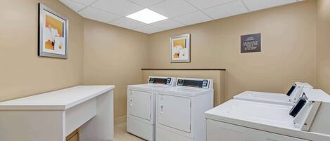 A laundry room with two front-loading washers and dryers, a white counter, and two framed pictures on the walls.