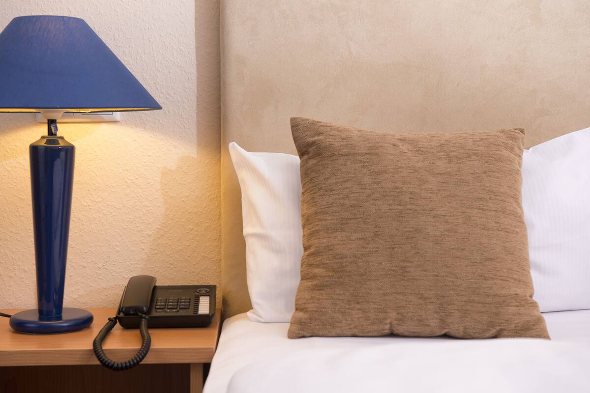 Una habitación de hotel con cama, una lámpara azul, un teléfono y un almohadón marrón.