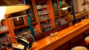 A bar area with shelves of glasses and bottles, wooden bar counter, and hanging lamps. - TRYP by Wyndham Bremen Airport (Bremen)