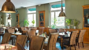 A restaurant with multiple tables and chairs, large windows, and hanging pendant lights. - TRYP by Wyndham Bremen Airport (Bremen)
