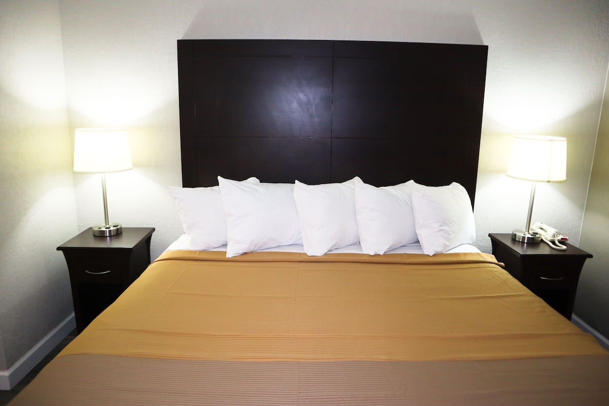 A hotel room with a large bed, two bedside tables with lamps, and a dark headboard.