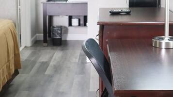 A hotel room with a bed, a desk with a lamp, a chair, a TV, and a bathroom visible in the background.