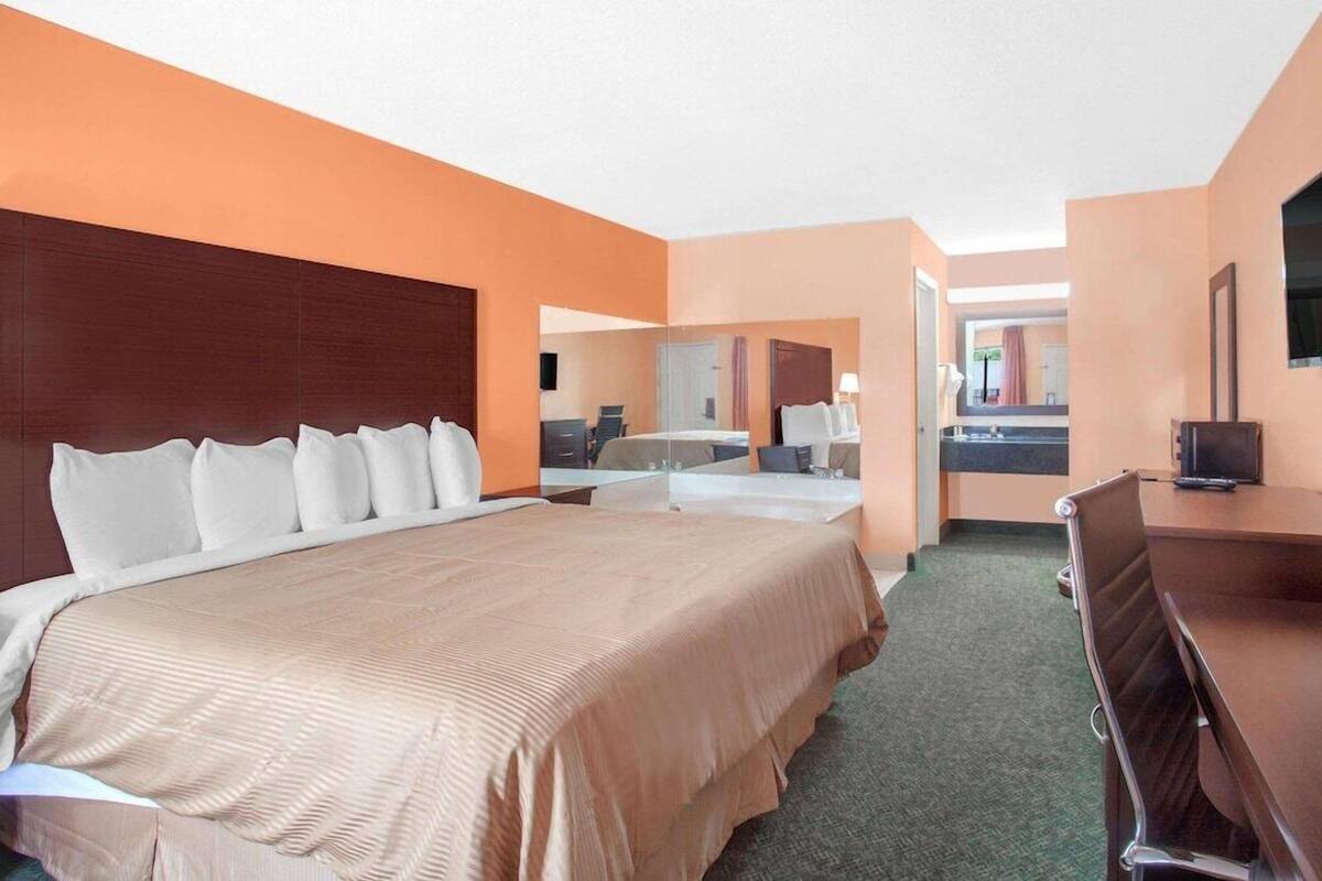 A hotel room with a large bed, a desk, a chair, and a mirror.