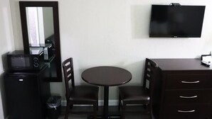 A compact hotel room with a single round table, two chairs, a small black refrigerator, a microwave, a TV mounted on the wall, and a dark wooden dresser with drawers. - Days Inn by Wyndham Moulton (Moulton)