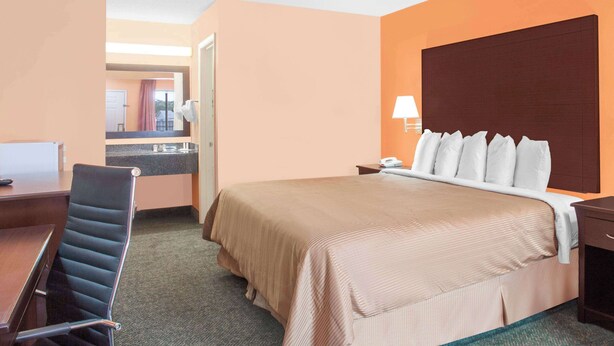 A hotel room with a bed, a desk, a chair, a nightstand, and a lamp. - Days Inn by Wyndham Moulton (Moulton)