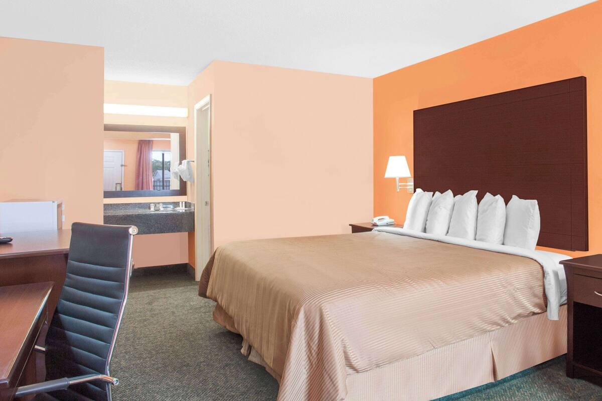 A hotel room with a bed, a desk, a chair, a nightstand, and a lamp.