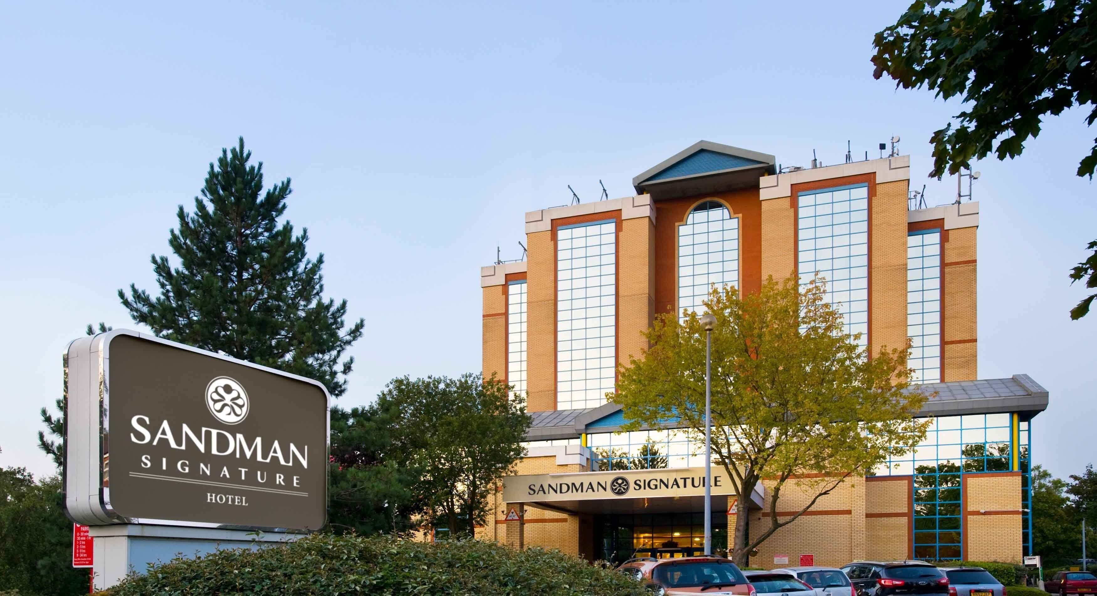 Un Hotel Sandman Signature con un letrero llamativo, ventanas amplias y un estacionamiento.