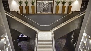 A modern hotel lobby with a central staircase, potted plants, and a reception desk.