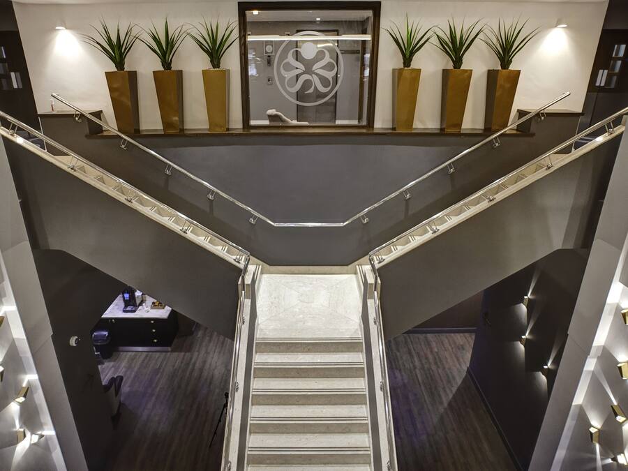 A modern hotel lobby with a central staircase, potted plants, and a reception desk.