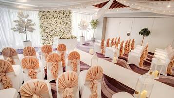 Un salón de bodas con hileras de sillas blancas, cubresillas color beige y cortinas blancas.
