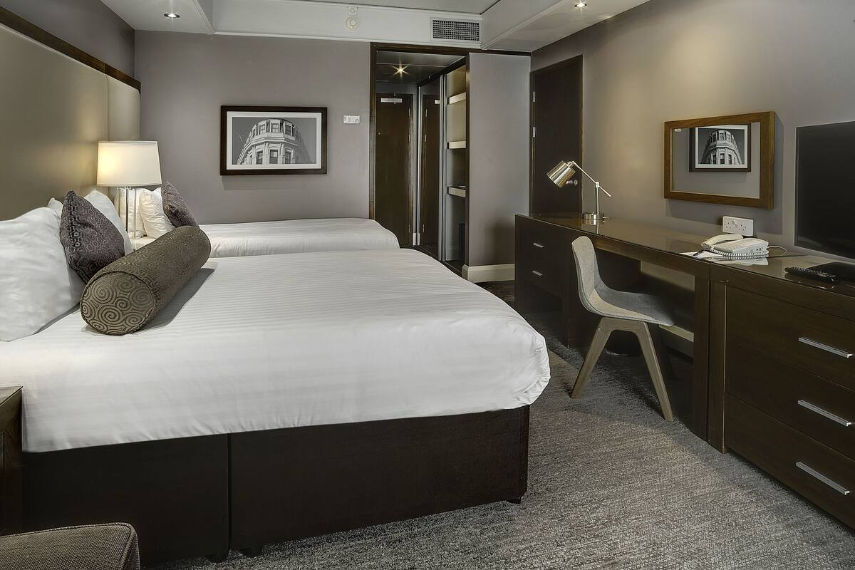 A hotel room with two beds, a desk, a chair, and a television.