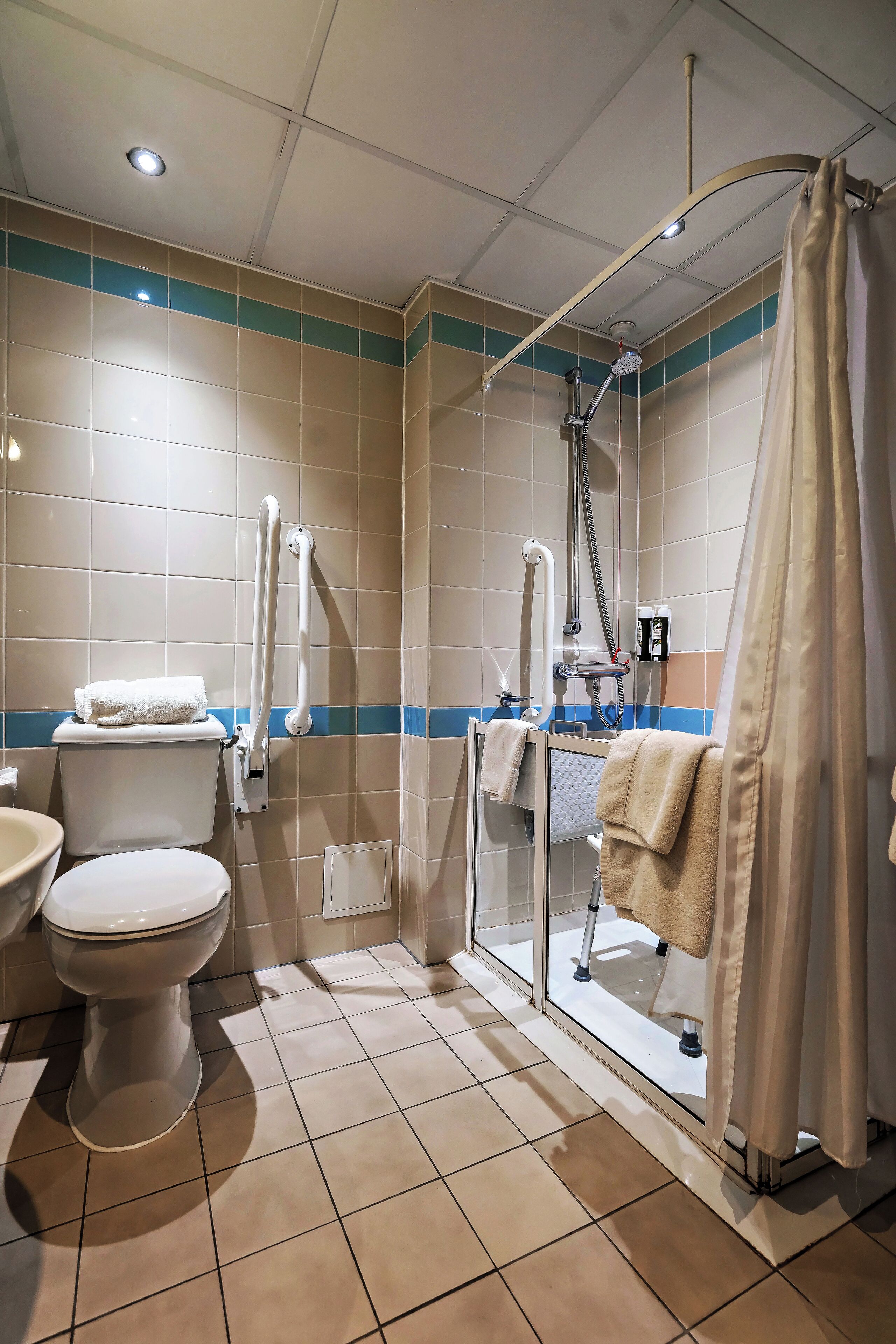 A bathroom with a toilet, a sink, a shower with a glass door, and a towel hanging on the wall.