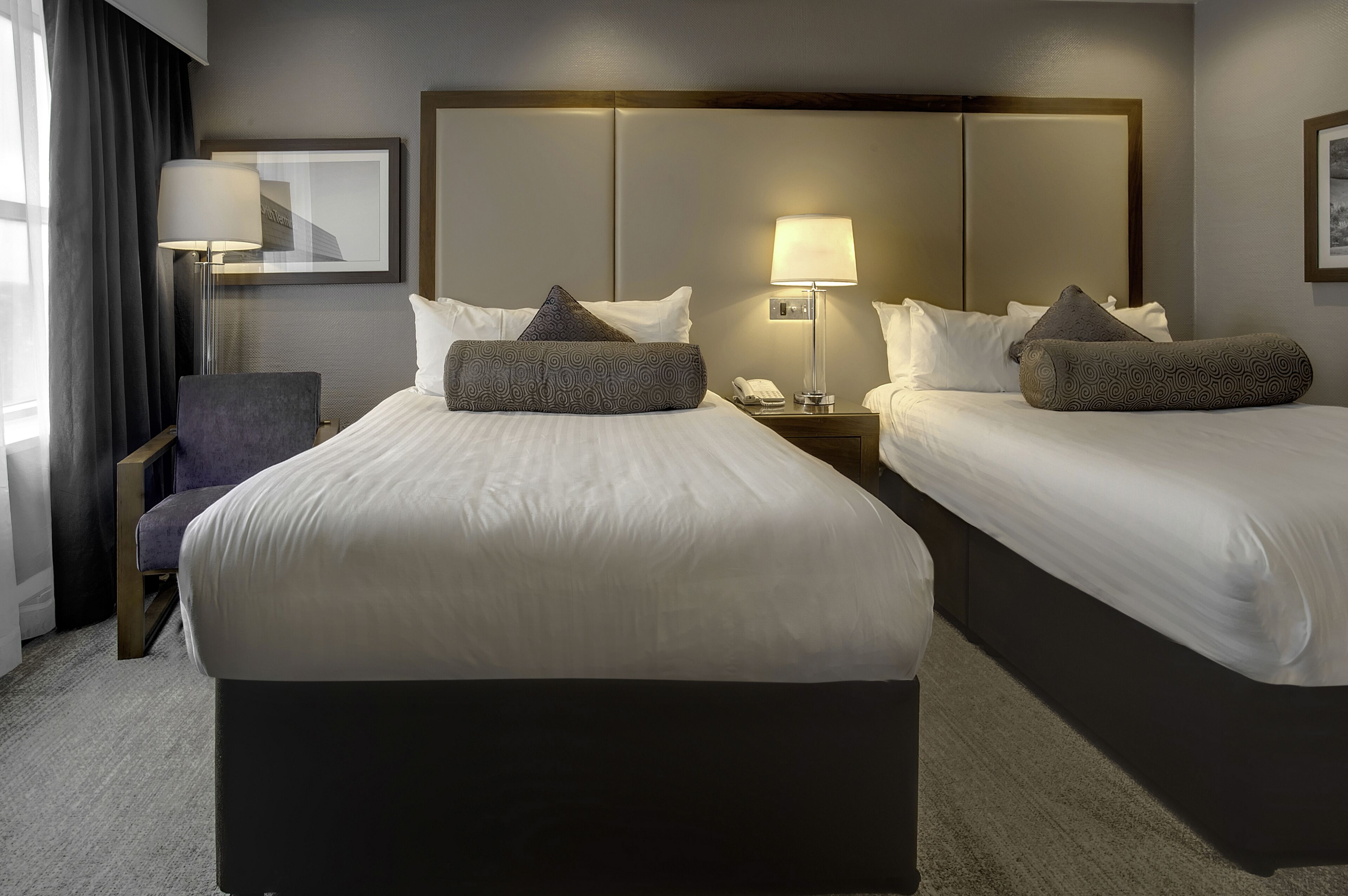Habitación de hotel con dos camas, una silla, un escritorio y una lámpara.
