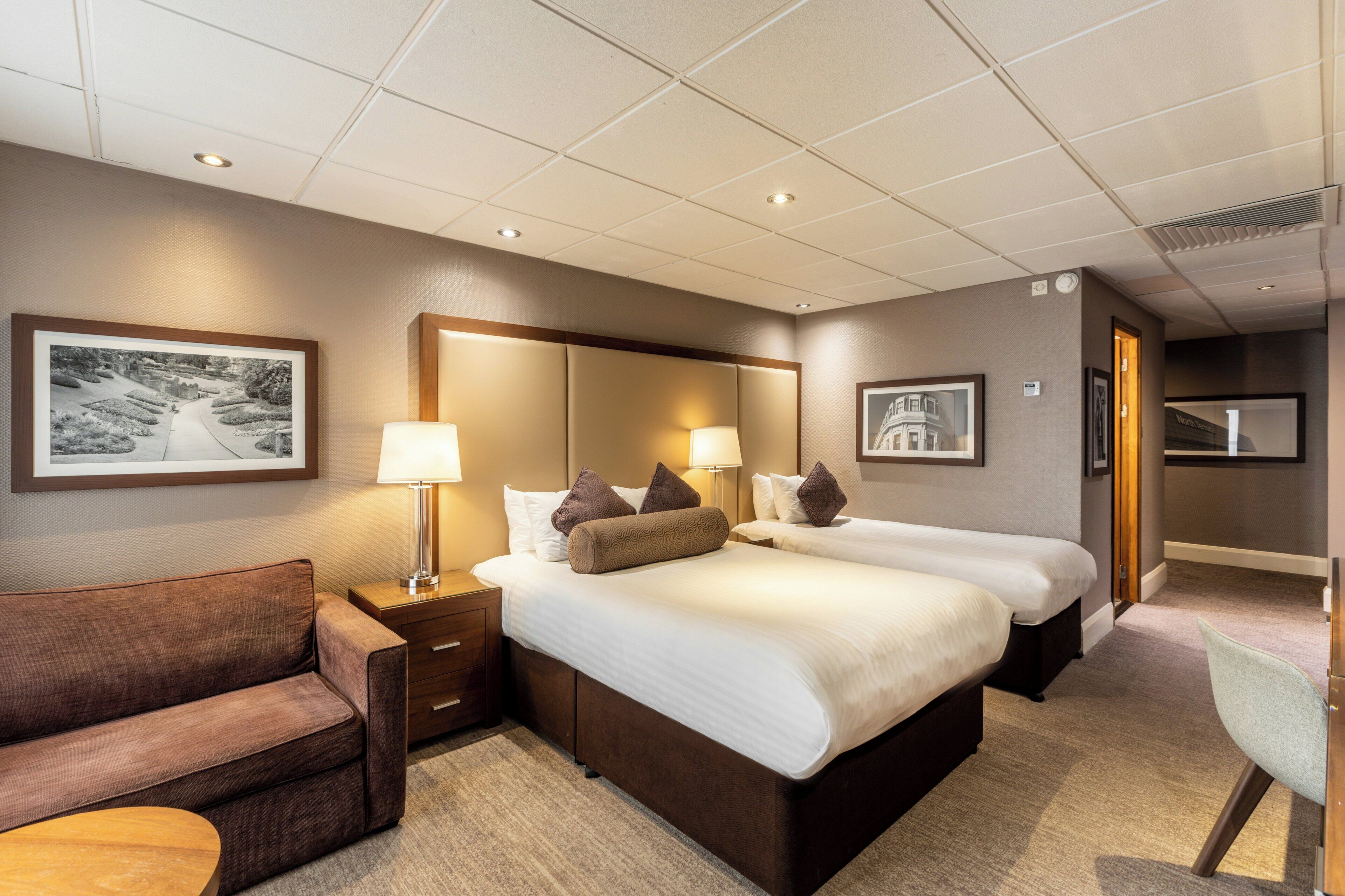 Ein Hotelzimmer mit zwei Betten, einem Sofa, einem Schreibtisch und einem Fernseher.