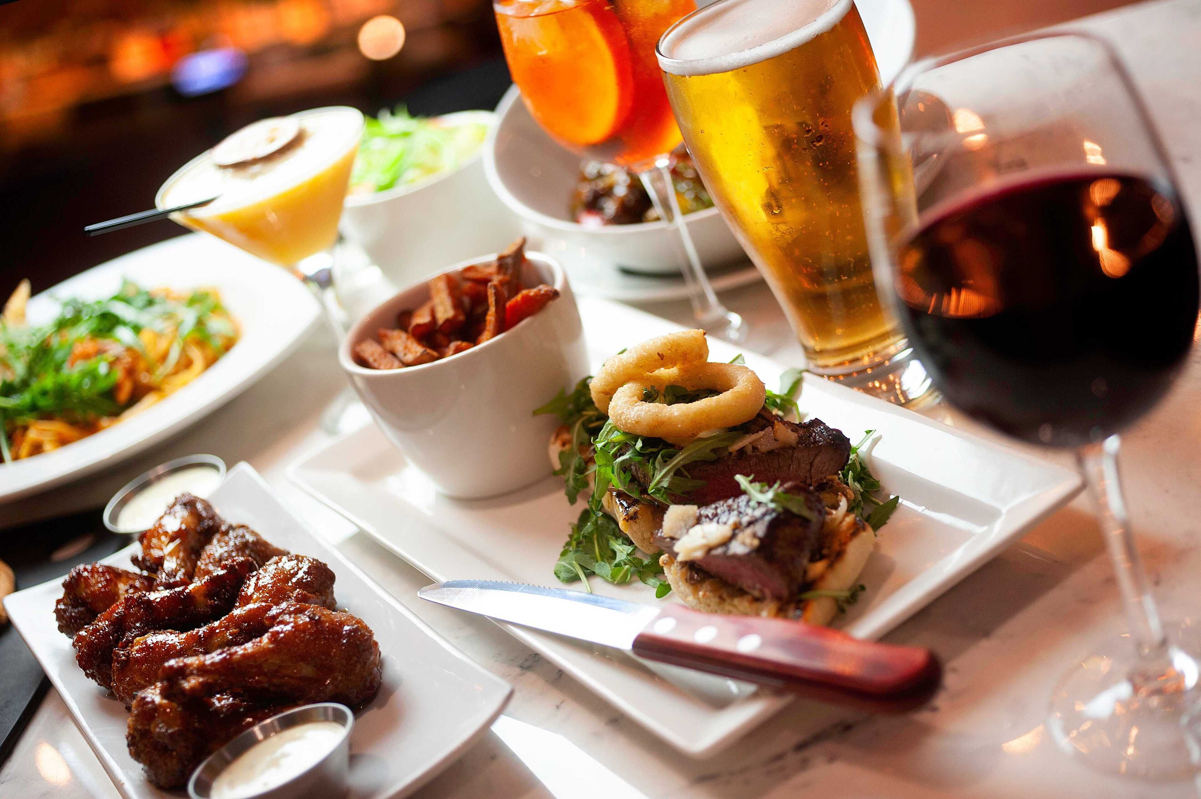 A variety of dishes including wings, a burger, and a salad, along with different types of drinks.