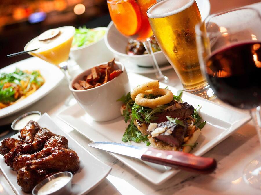 A variety of dishes including wings, a burger, and a salad, along with different types of drinks.