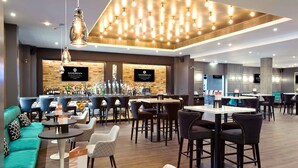 A modern bar area with a wooden wall, multiple seating options including sofas and tables, and a variety of bar stools.