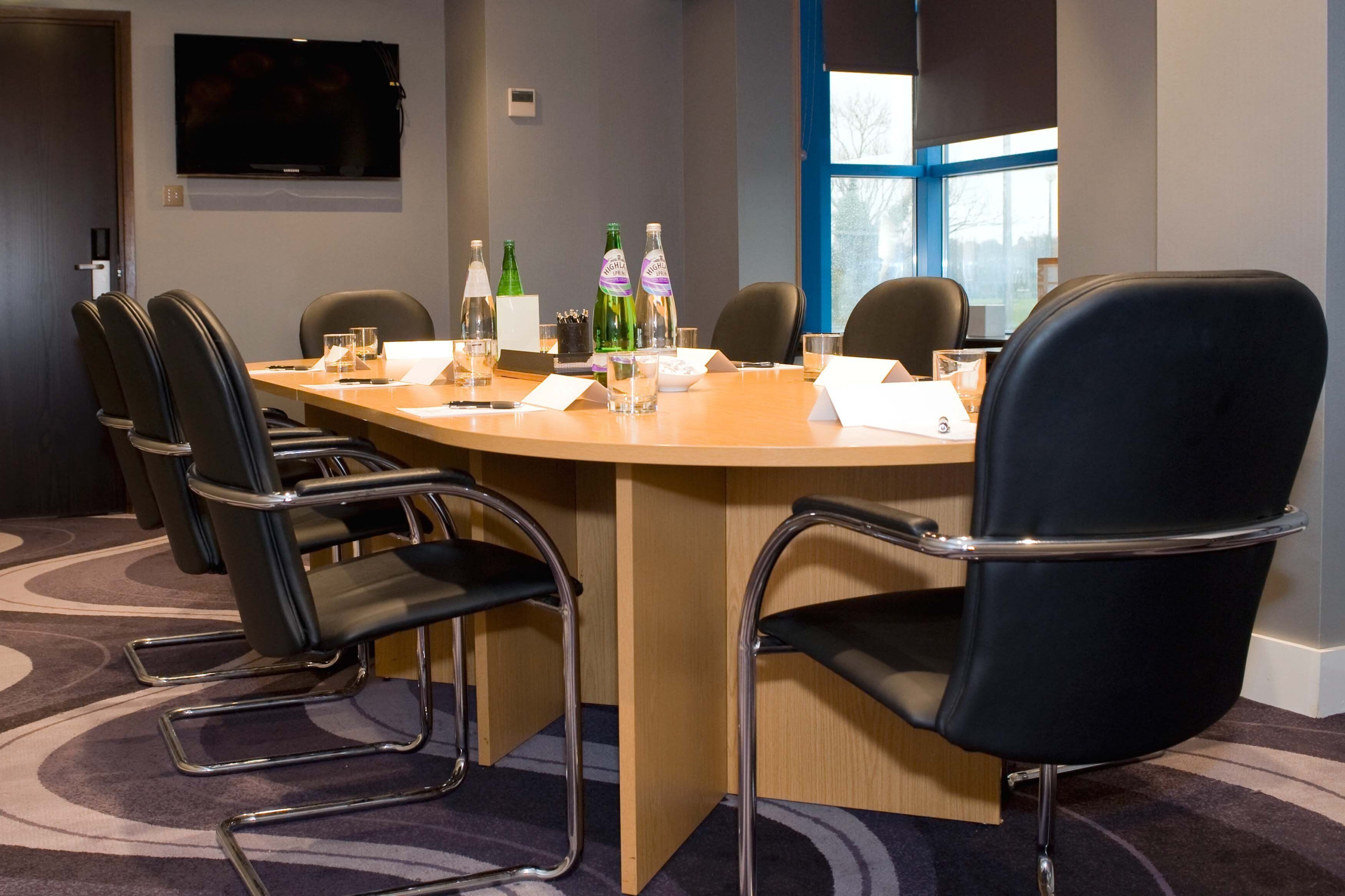 A conference room with a round table, black chairs, and a television on the wall.