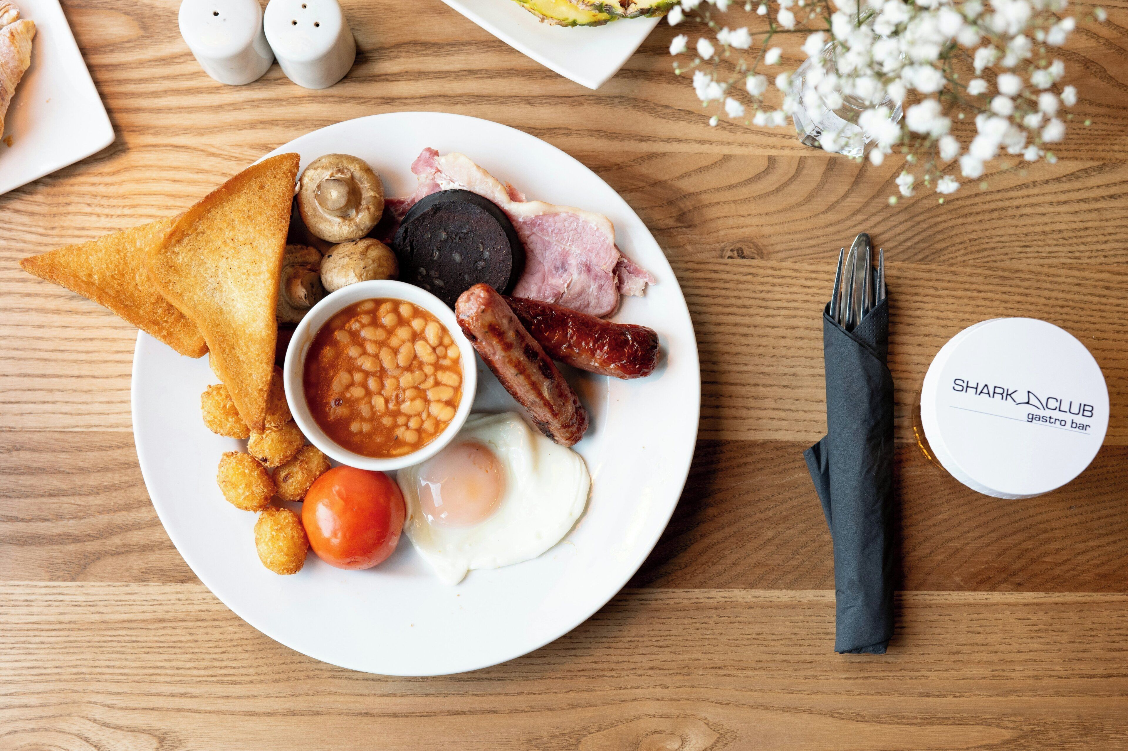 A plate of breakfast food including toast, eggs, sausages, mushrooms, beans, and a tomato.