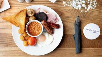 A plate of breakfast food including toast, eggs, sausages, mushrooms, beans, and a tomato.