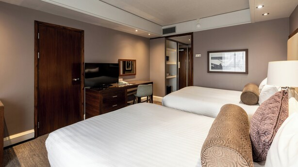 A hotel room with two beds, a desk, a television, and a wardrobe.