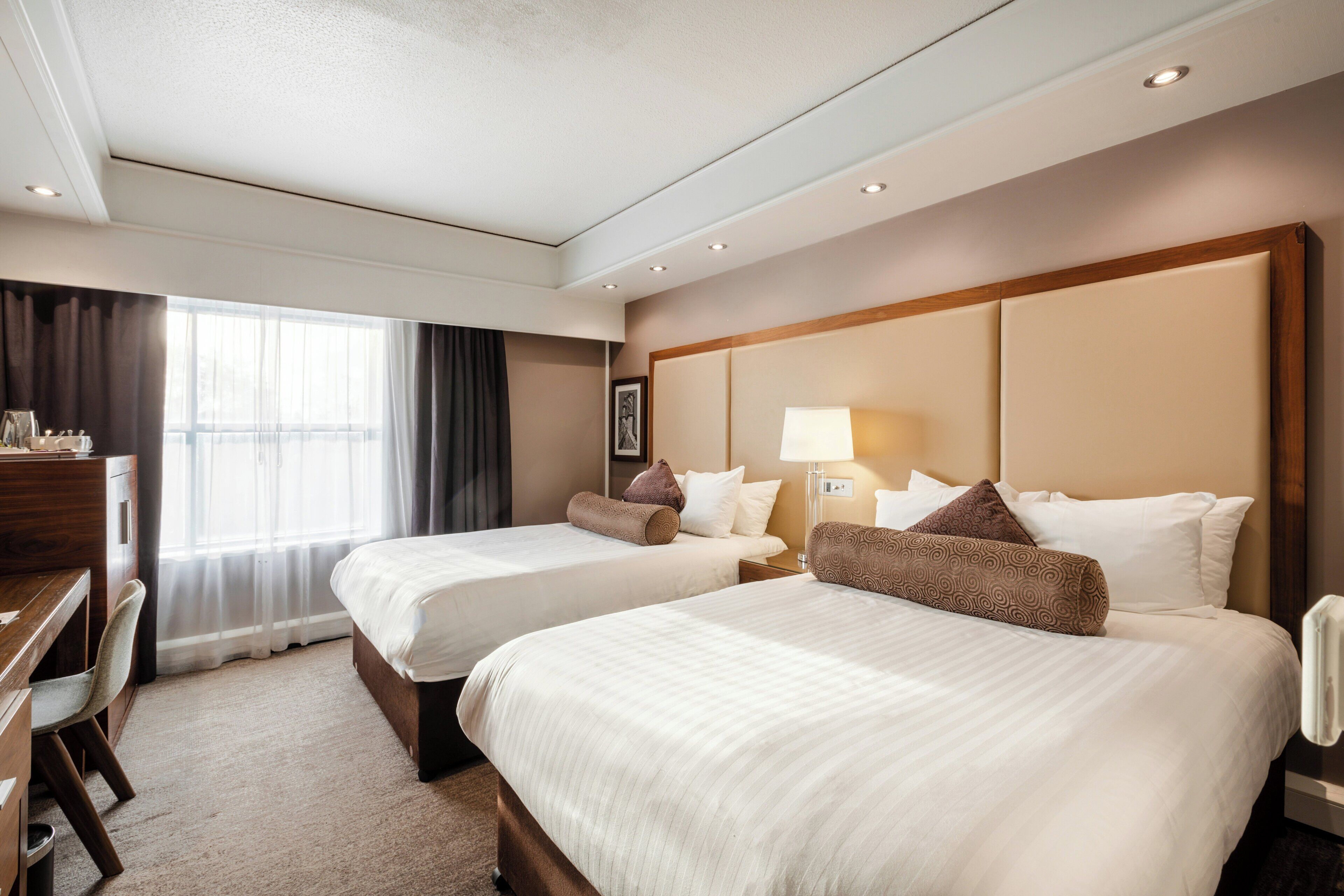 Ett hotellrum med två sängar, ett skrivbord och ett stort fönster.