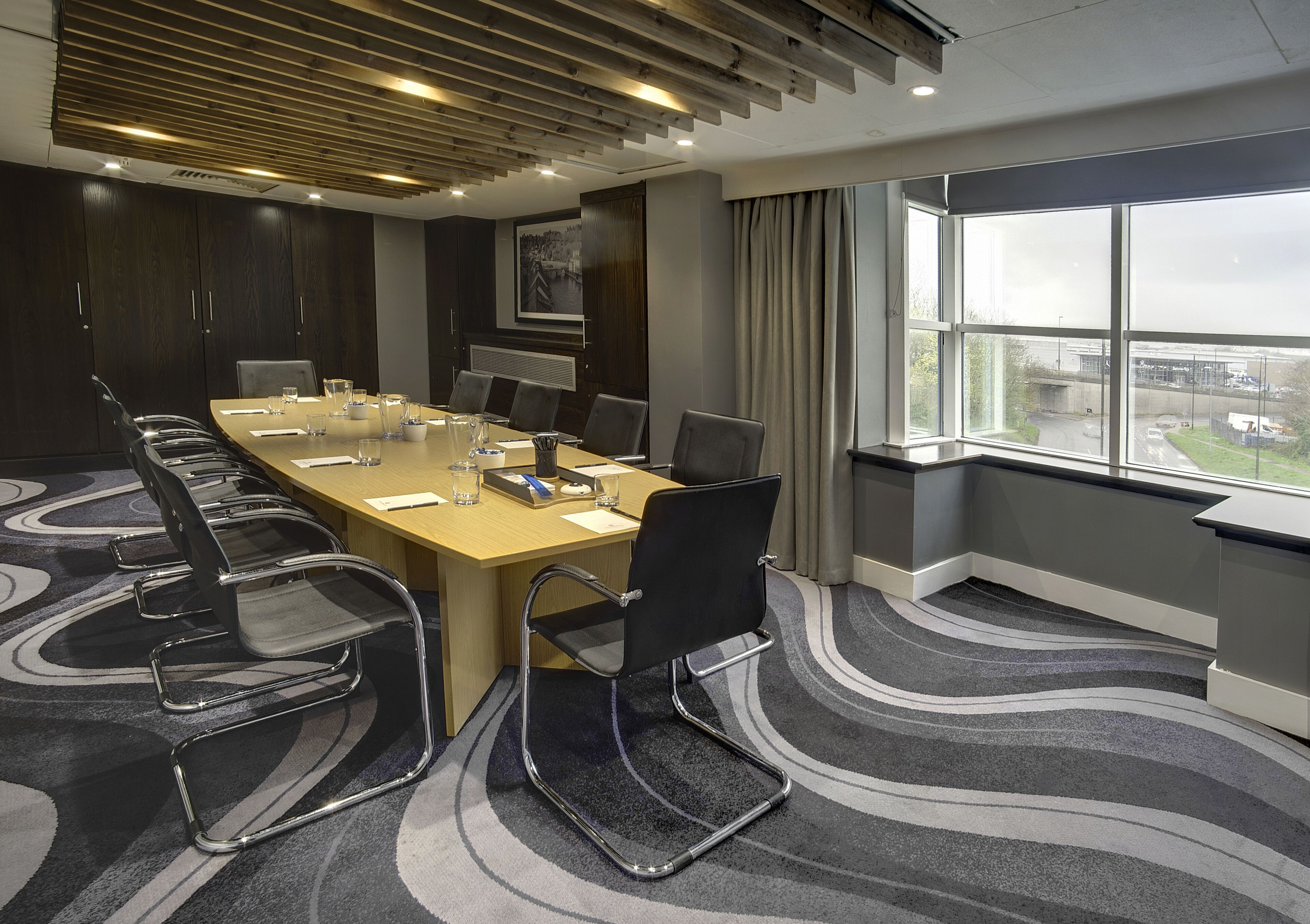 A conference room with a long table, chairs, and a view through large windows.